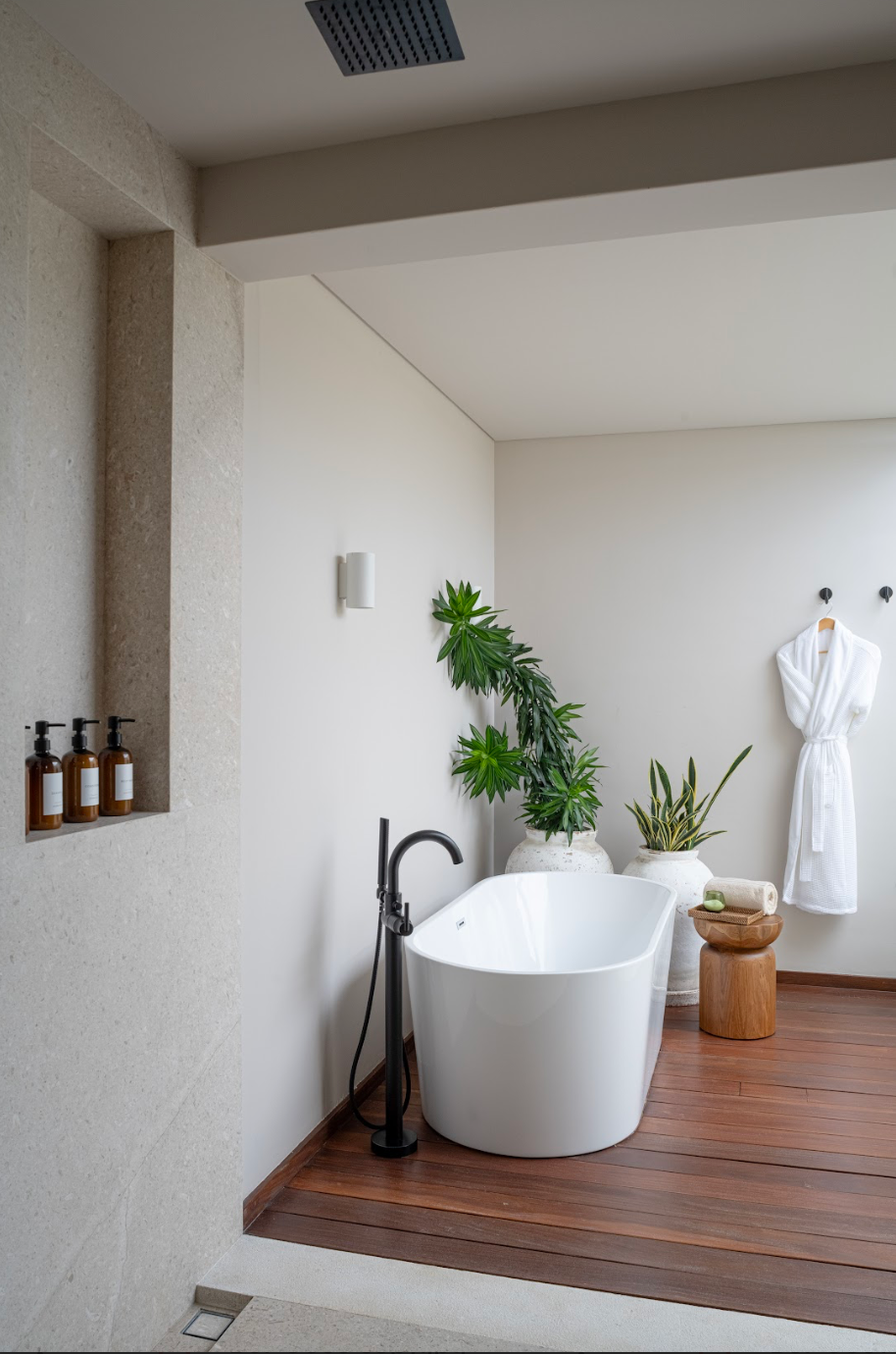 Modern bathroom with a freestanding bathtub, plants, and a robe.